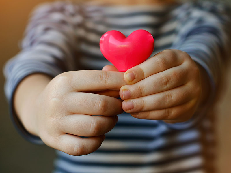 young child holding a small pink heart out in front of them