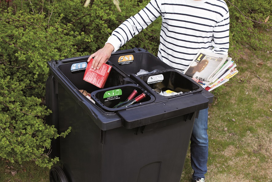 Photo showing a person sorting recycling into a large black wheelie bin divided into four compartments.