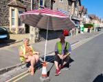Two people sat under a sun umbrella in the street