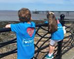 A boy and girl wearing North Somerset Fostering branded t-shirts standing by railings looking out towards Clevedon Pier