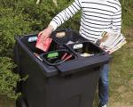 Photo showing a person sorting recycling into a large black wheelie bin divided into four compartments.