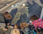 Five children playing together and drawing with chalk on a road