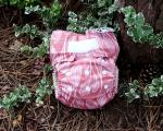 A pink patterned reusable nappy is positioned against a tree trunk, with leaves in the background