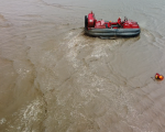A red hovercraft heads towards a dummy that's stuck in the mud, as the tide comes in