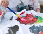 A child uses a paintbrush to swirl colourful paint on a white t-shirt