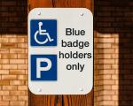 A white sign attached to a wooden post reads 'Blue badge holders only'