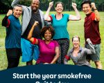 A group of six people of various ages in a park, each with a hand raised in celebration of better health as a result of stopping smoking