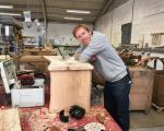 A photo of Tom Palmer, Director of Somerset Wood Recycling, leaning against a piece of wood furniture in a carpentry workshop