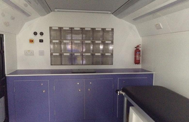 An inside view of MAVIS bus with a purple counter and bench, with storage drawers on the wall