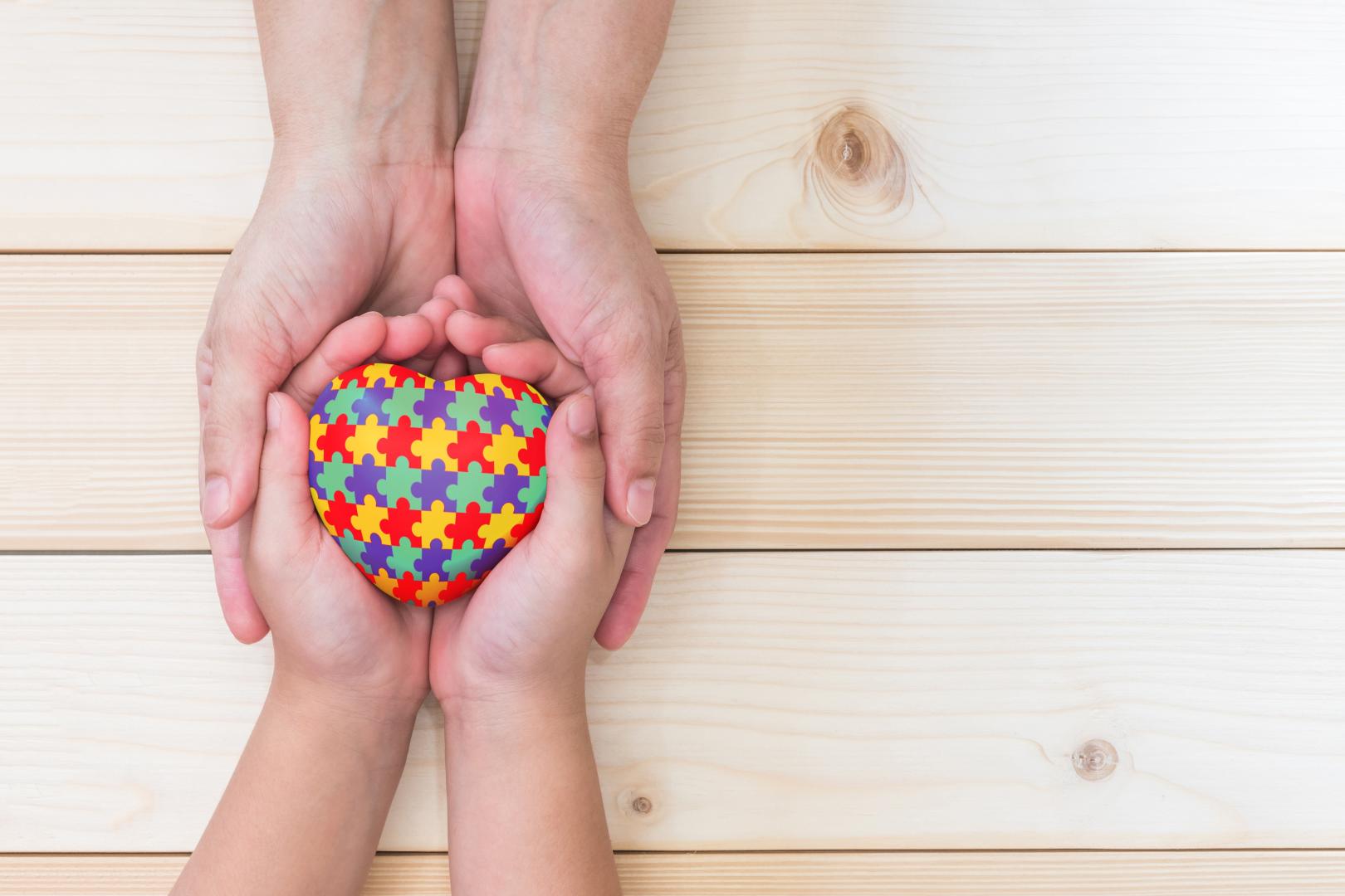 adult's hands holding child's hands with a multi-coloured jigsaw heart