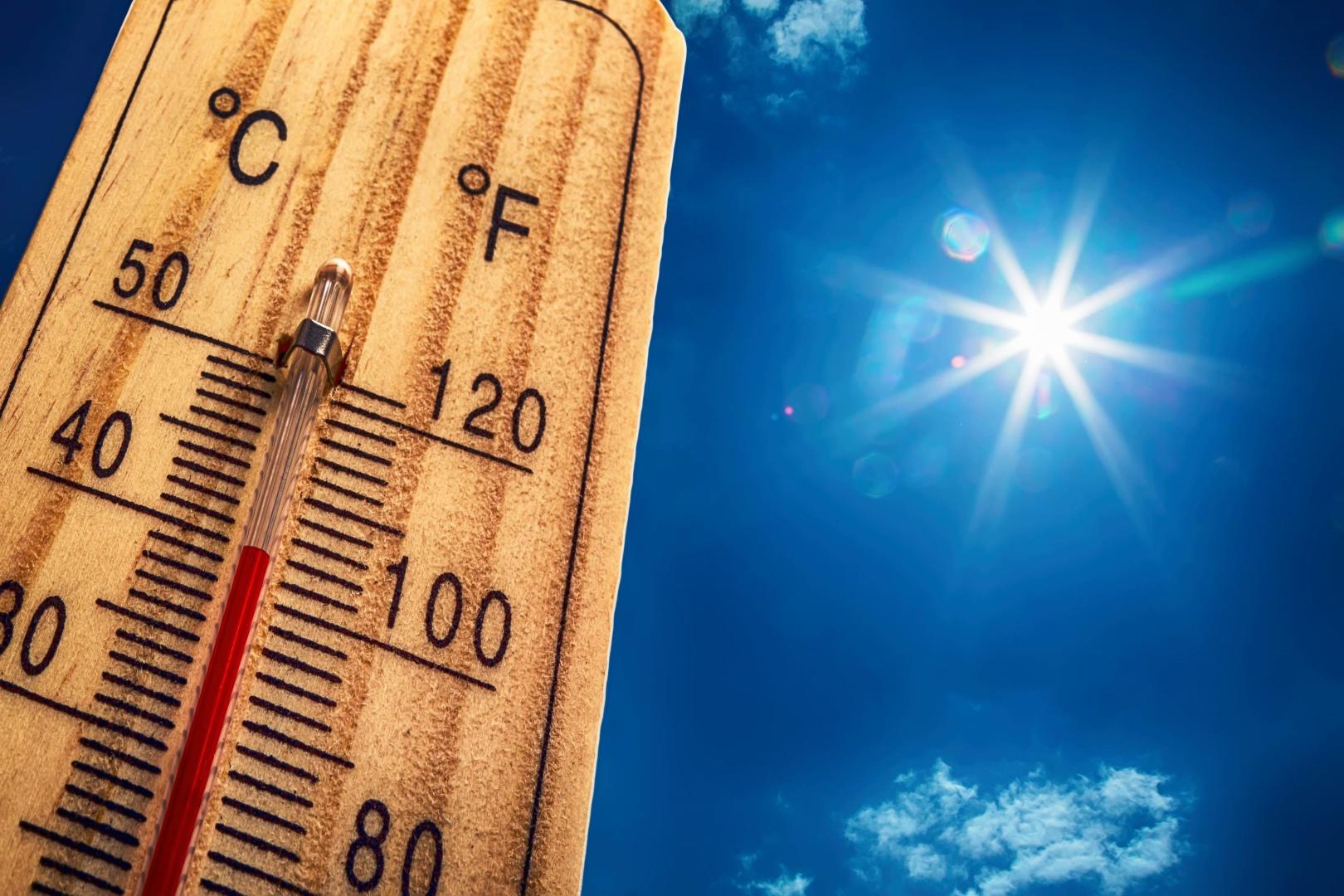 A thermometer against a blue sky with a hot sun