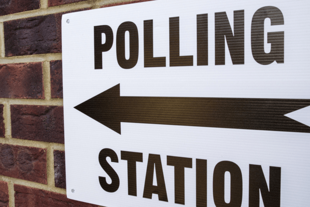 Sign on brick wall that reads 'Polling Station' with a directional arrow pointing left.