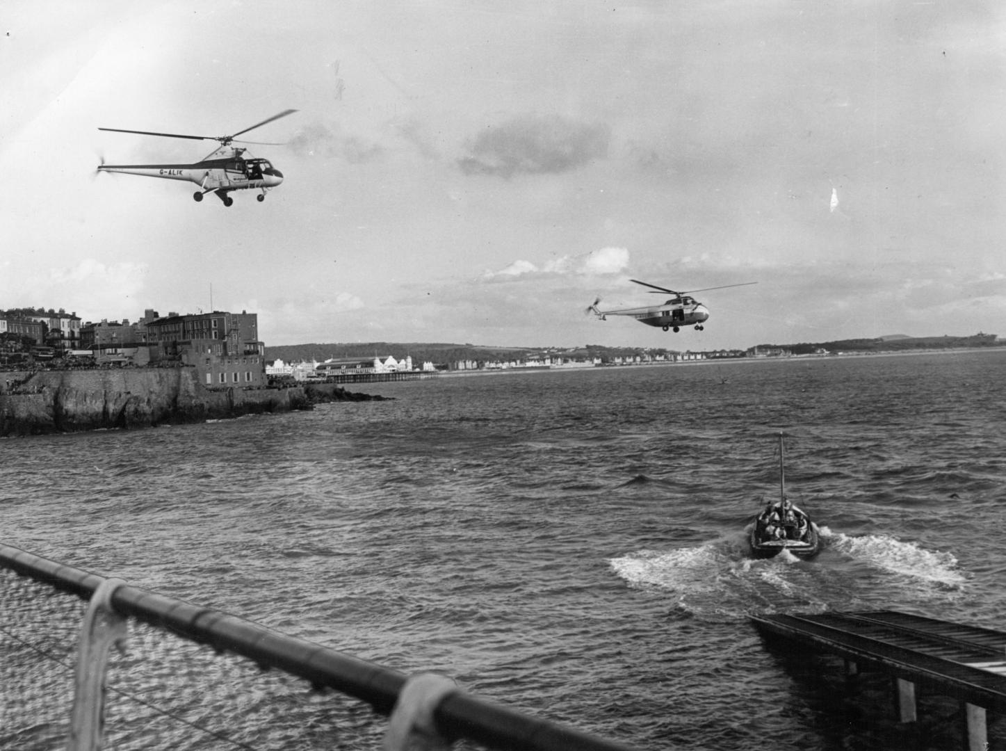A historical photo of the RNLI lifeboat launching off Birnbeck Pier with two helicopters flying overhead at the same time.