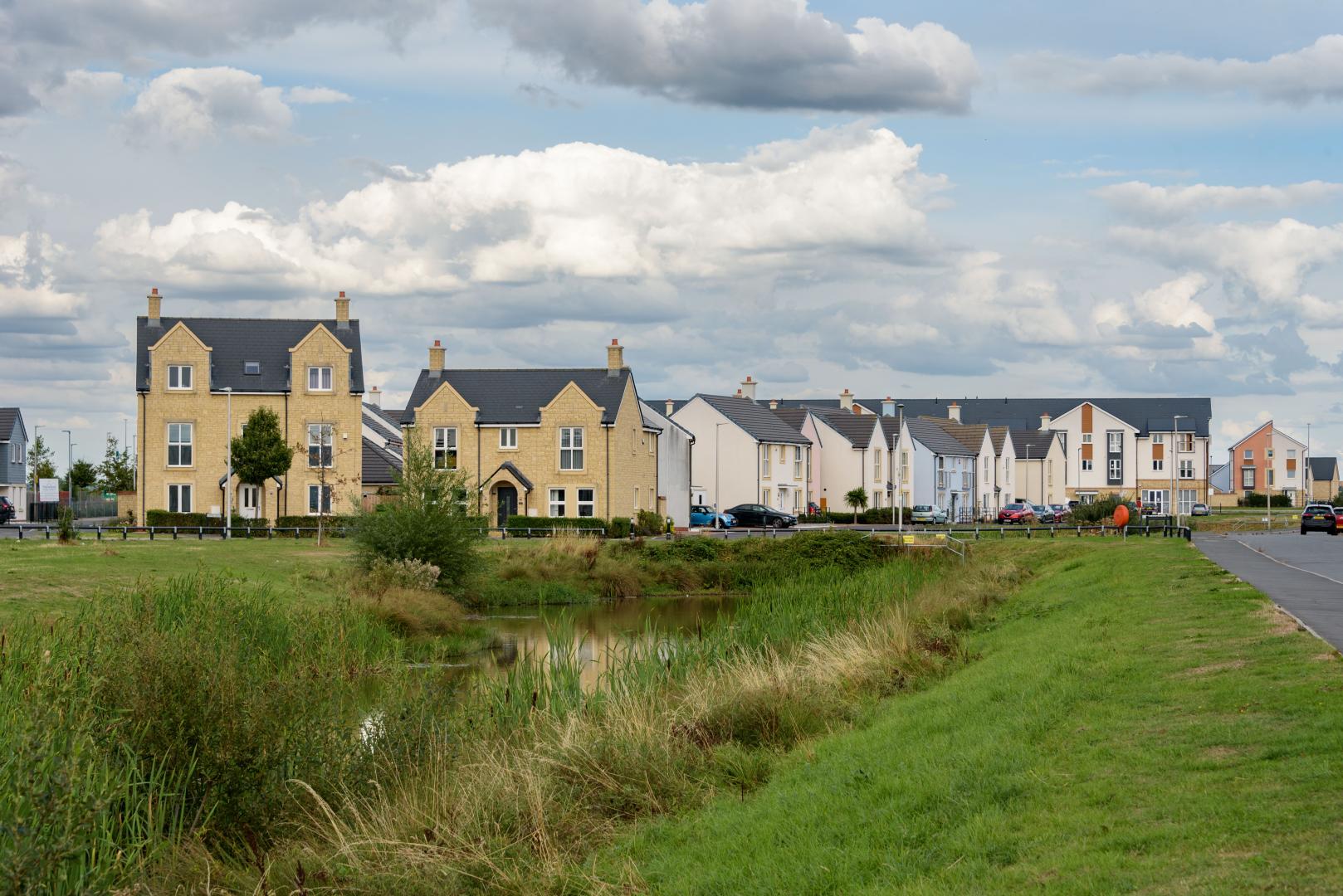A row of houses, with a pond and green space in front of them