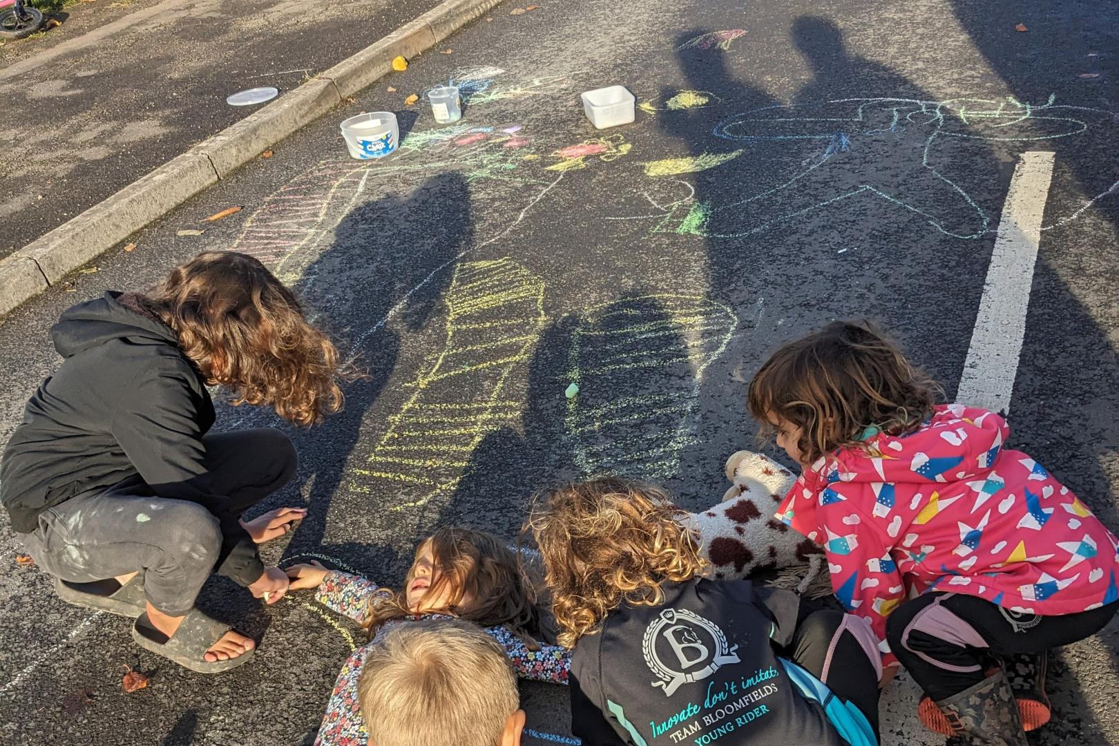 Five children playing together and drawing with chalk on a road