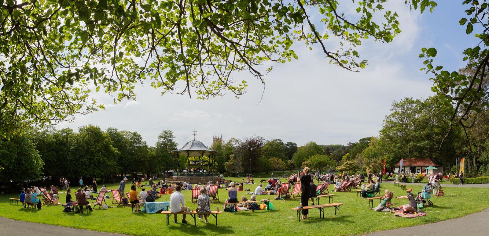 A wide angle shot of Grove Park, a vast green space dotted with people with a Victorian bandstand visible to the left and trees hanging overhead. Image by Paul Blakemore.