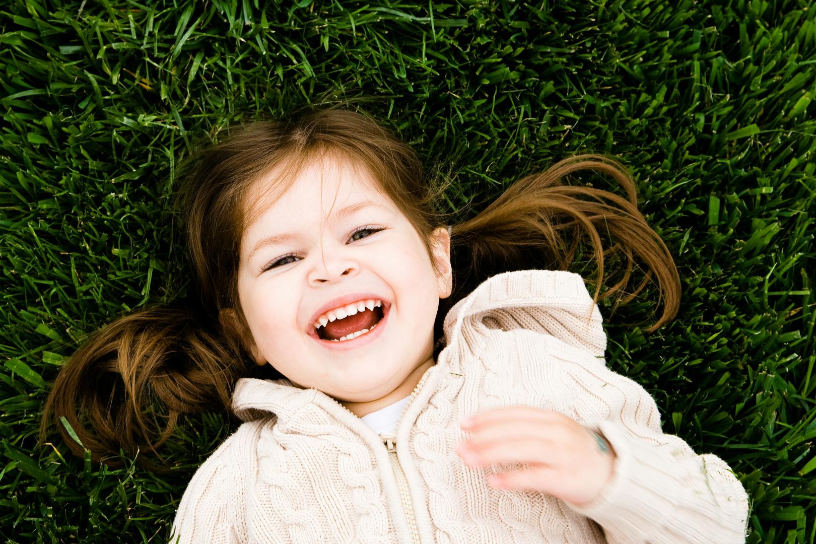 A girl dressed in a white hoodie lies on the grass and smiles at the camera 