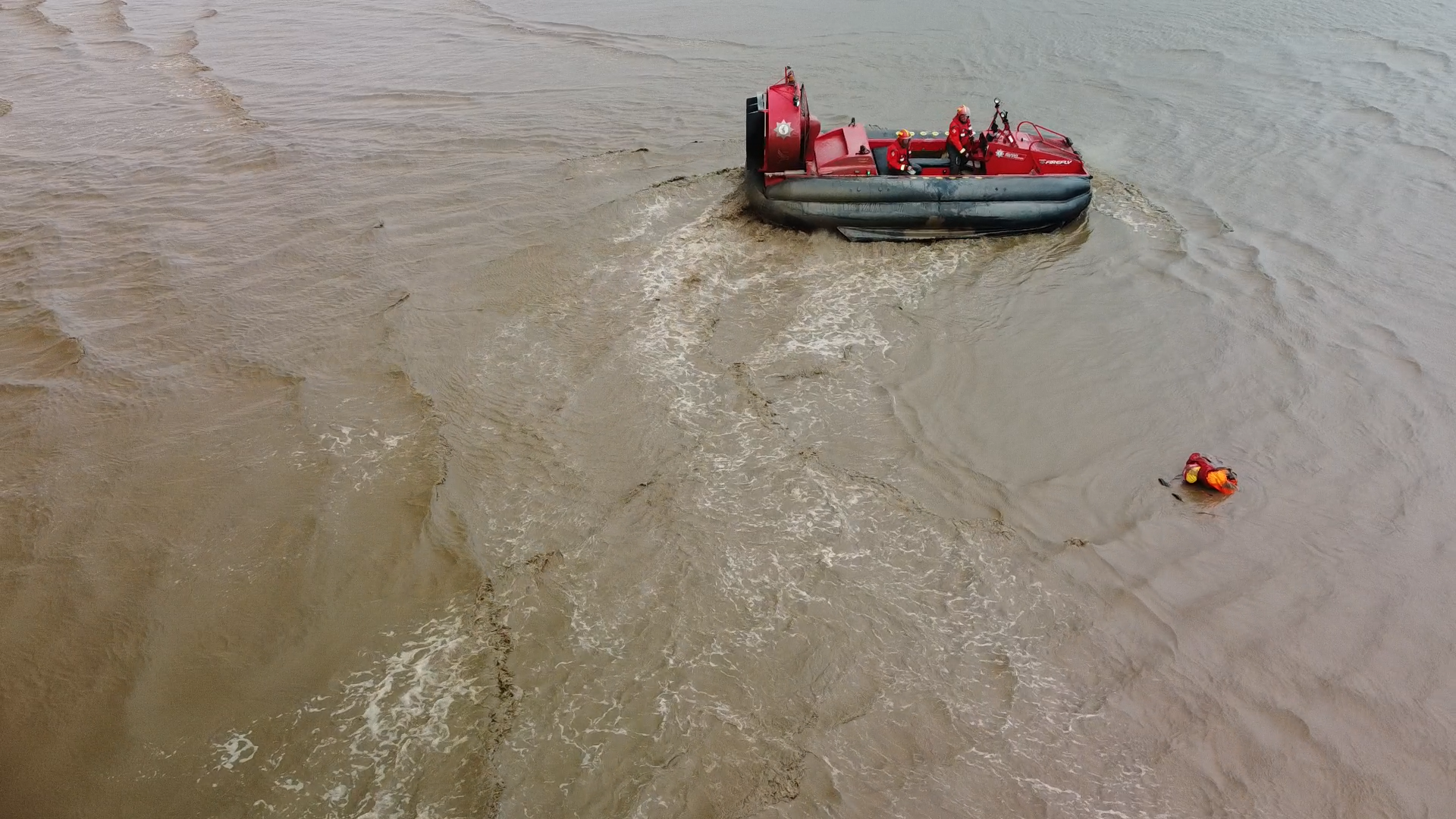 A red hovercraft heads towards a dummy that's stuck in the mud, as the tide comes in