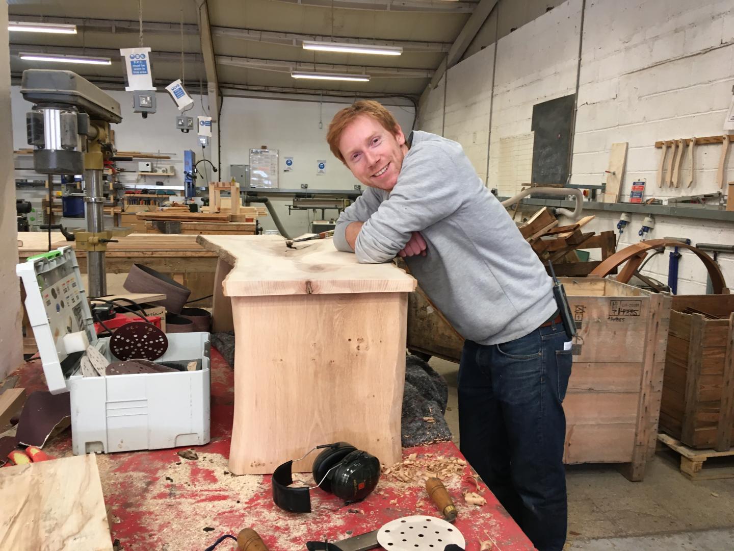 A photo of Tom Palmer, Director of Somerset Wood Recycling, leaning against a piece of wood furniture in a carpentry workshop