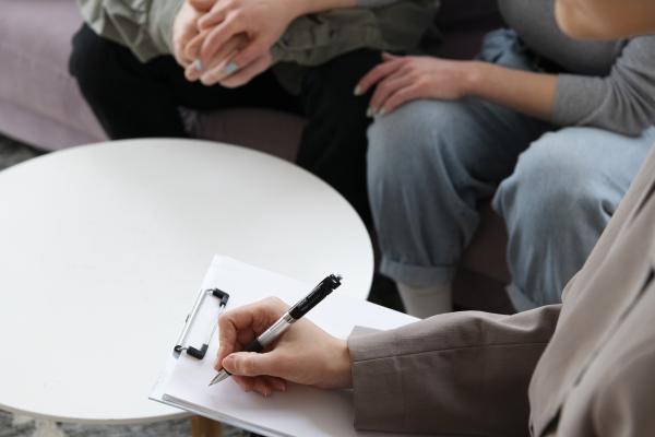 Freepik - an overhead photo of a round white table, with three people sitting around it (just showing their legs). Someone has a notepad on the table and is writing.