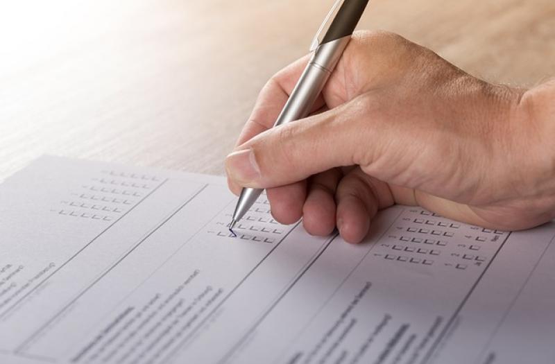 A hand filling out a paper questionnaire with a pen