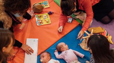 two babies laid on play mats with their parents say round them