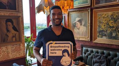 Gagandeep holding a Breastfeeding Welcome sign and smiling at the camera